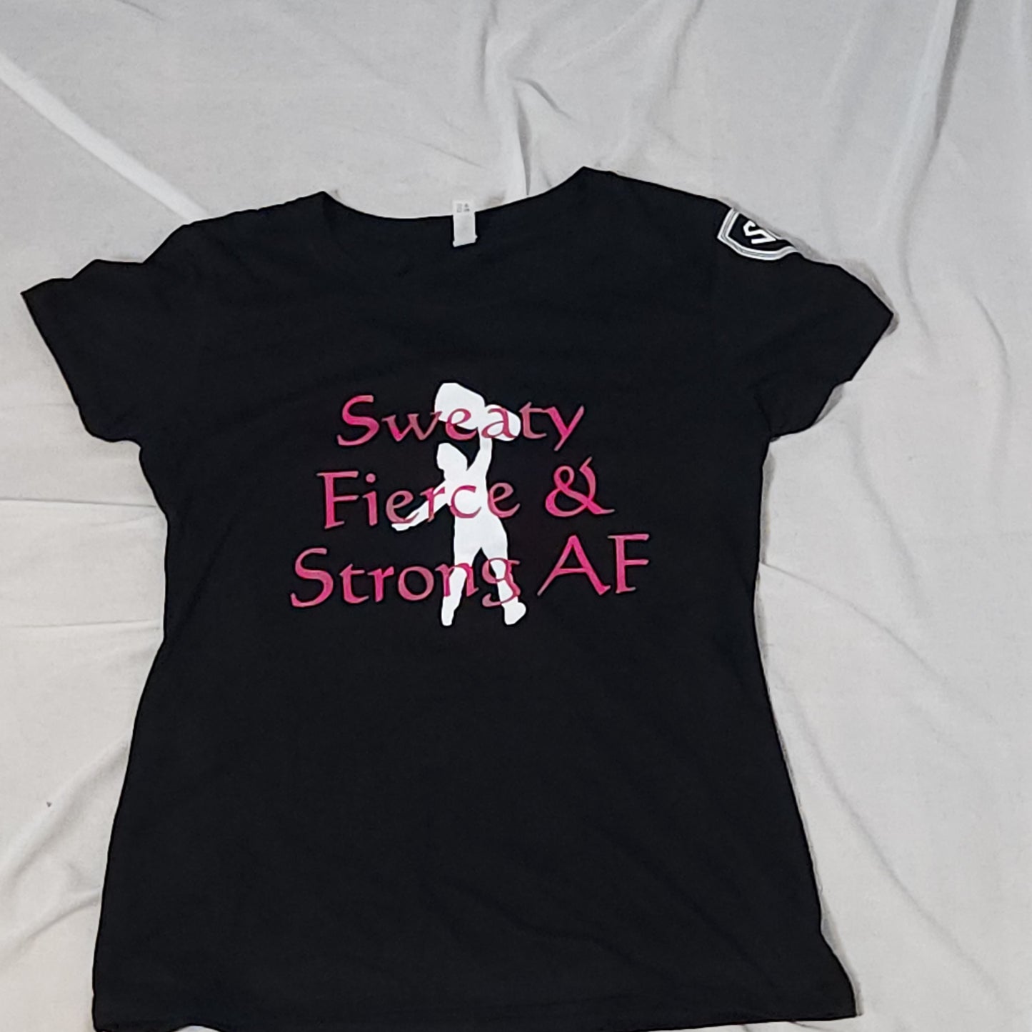 Black Strongbox Apparel Ladies' Cut Tee with hot pink lettering and white graphic on the front, featuring the Strongbox Apparel crest on the sleeve. Tee is called 'Sweaty Fierce and Strong AF' and is available in sizes small through 2X. Designed to keep you comfortable and stylish during workouts.