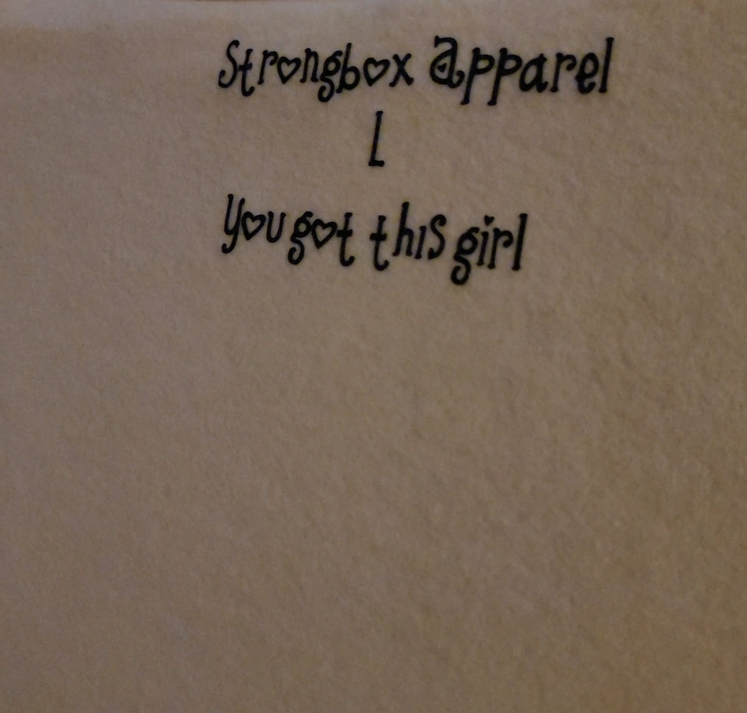 A close-up of a motivational size tag that reads "you got this girl". The text is in bold, black font with a feminine script style. The tag is designed to provide constant motivation and empowerment to the wearer of the Strongbox Apparel "Just a Girl Who" Collection Crop Hoodie